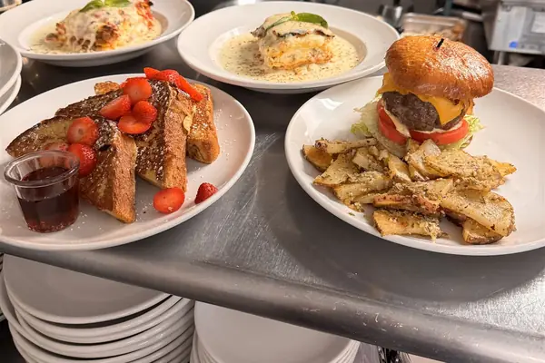 Brunch plates on the kitchen pass: French toast with strawberries and a burger with home fries