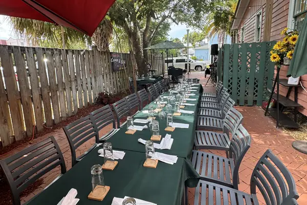 Courtyard set for a private party: long tables with green tablecloths under string lights and shade trees
